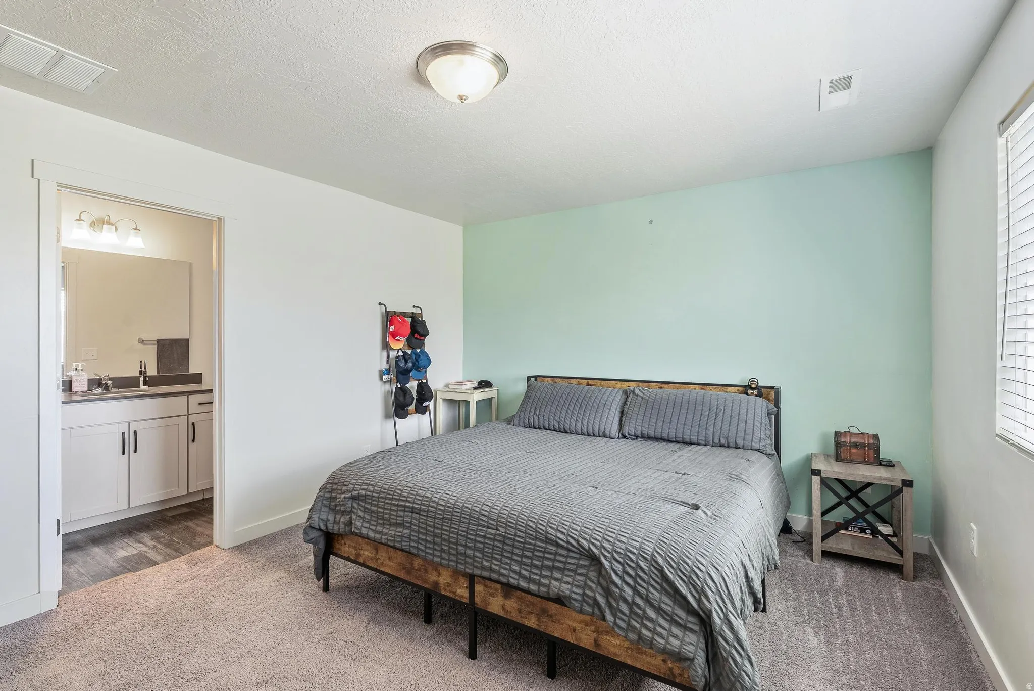 Carpeted room featuring a light aqua accent wall and a window with horizontal blinds