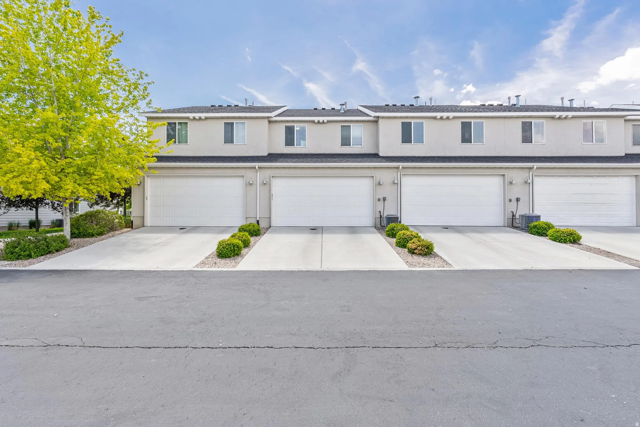 Modern townhome exteriors featuring light-colored stucco, white garage doors, and individual concrete driveways