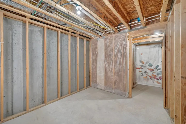 Unfinished basement featuring concrete flooring, exposed wood framing, and an exposed ceiling with visible utilities