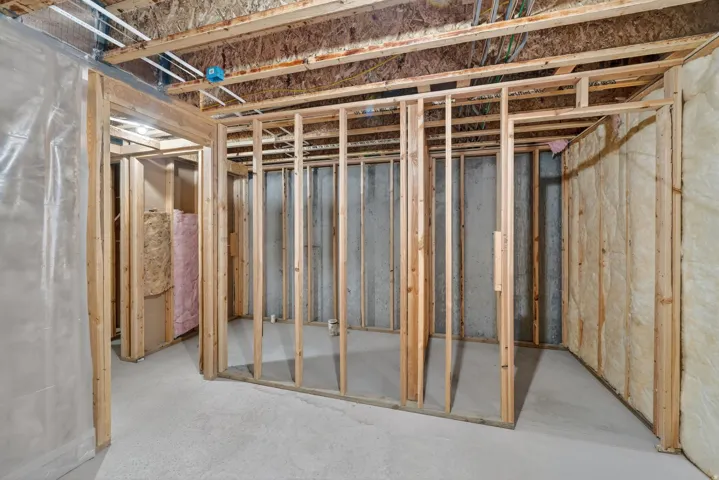 Unfinished basement space featuring exposed wood framing, concrete flooring, insulation, and visible ceiling joists