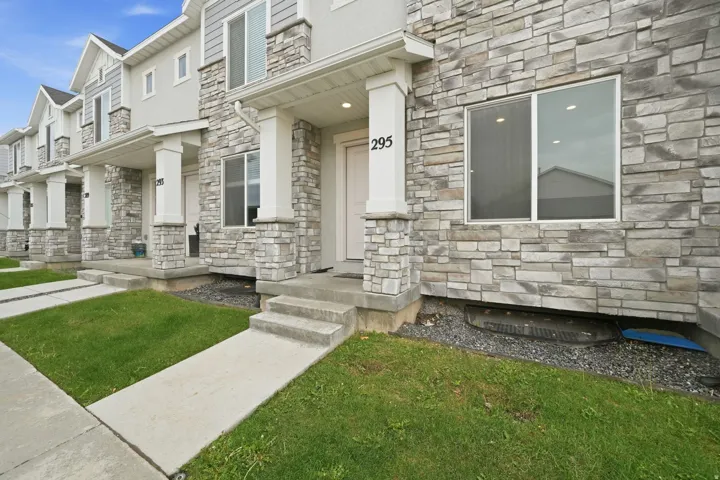 Exterior featuring a stone facade, covered porch entry, concrete steps, and a landscaped lawn