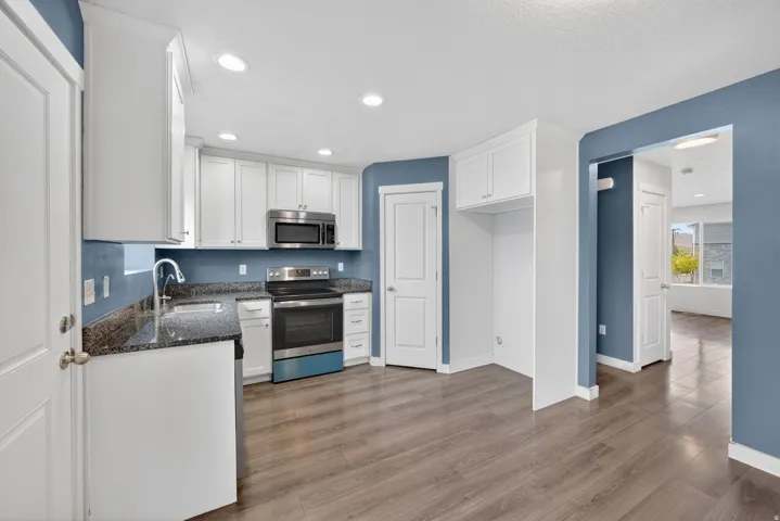 Kitchen featuring white cabinetry, stainless steel appliances, dark stone countertops, wood-finish flooring, and recessed lighting