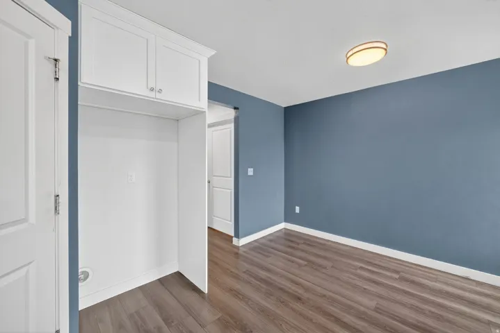 Built-in white cabinetry with polished hardware, contrasting accent wall, wood-finish flooring, white baseboards, and a flush-mount ceiling light fixture