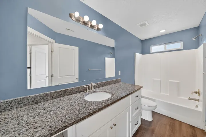 Bathroom featuring a white vanity with a granite-style countertop, undermount sink, and a large wall mirror