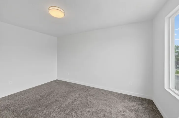 Neutral-toned interior room featuring light gray carpet, white walls, and a single window with white trim