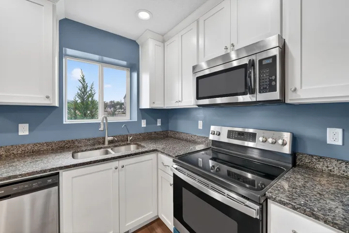 Kitchen featuring white cabinetry, granite-finish countertops, stainless steel appliances, and a double-basin sink with a gooseneck faucet