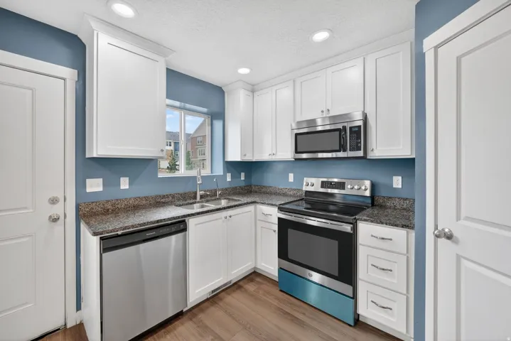 Modern kitchen featuring white cabinetry, stainless steel appliances, granite-style countertops, and wood-finish flooring