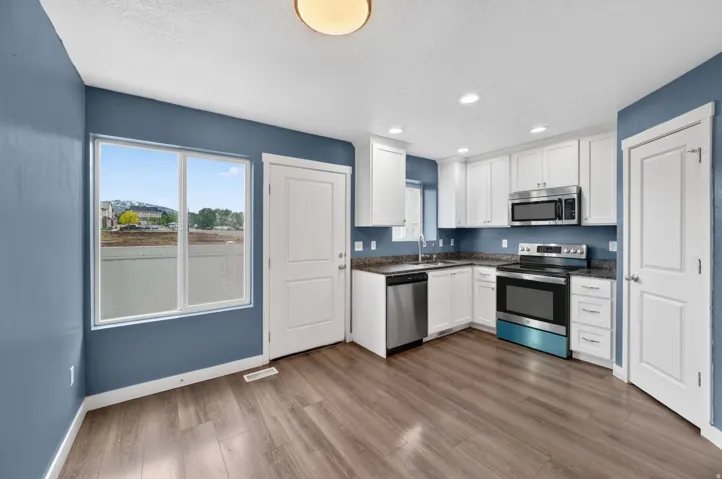 Kitchen featuring white cabinetry, stainless steel appliances, granite-finish countertops, and wood-finish flooring