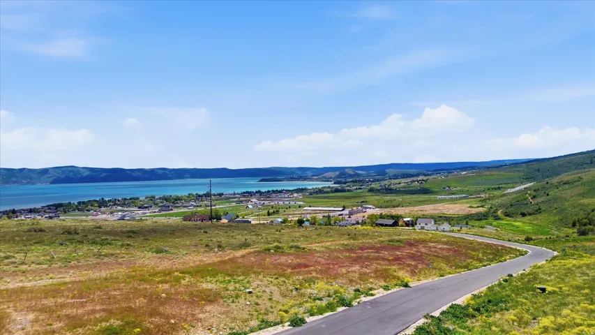 Expansive elevated lot featuring a paved road, undulating green hills, and distant water body