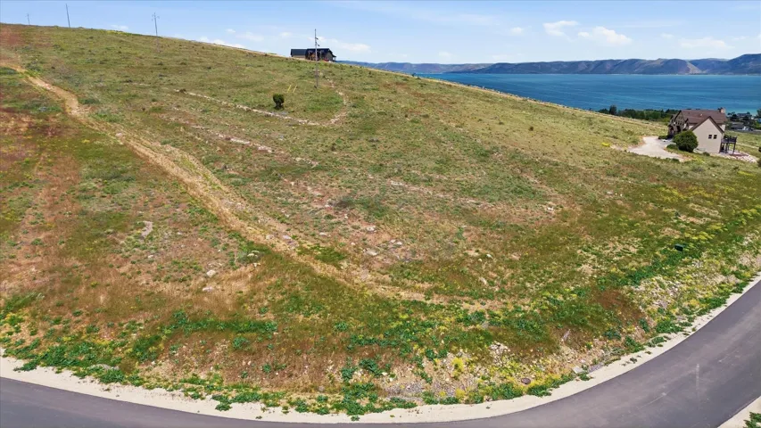 Sloping land parcel with a paved road frontage, offering distant water and mountain scenery