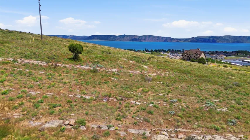 Expansive hillside property featuring natural vegetation, rocky outcrops, and distant water scenery