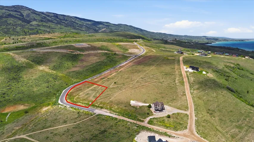 Elevated lot with mountain backdrop, featuring paved road access and distant water body