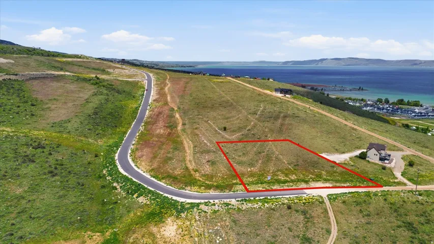Expansive hillside parcel featuring a defined lot boundary, paved road frontage, and distant lake scenery