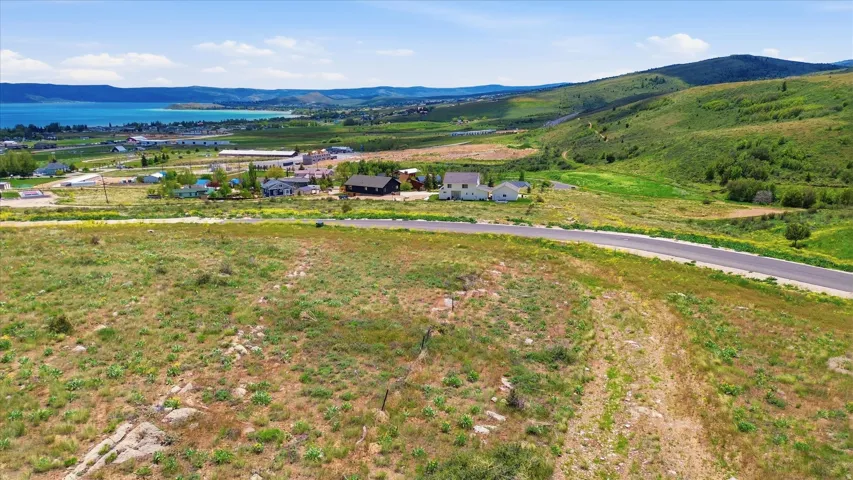Expansive land parcel featuring a paved road, scattered residences, and a substantial body of water in the background