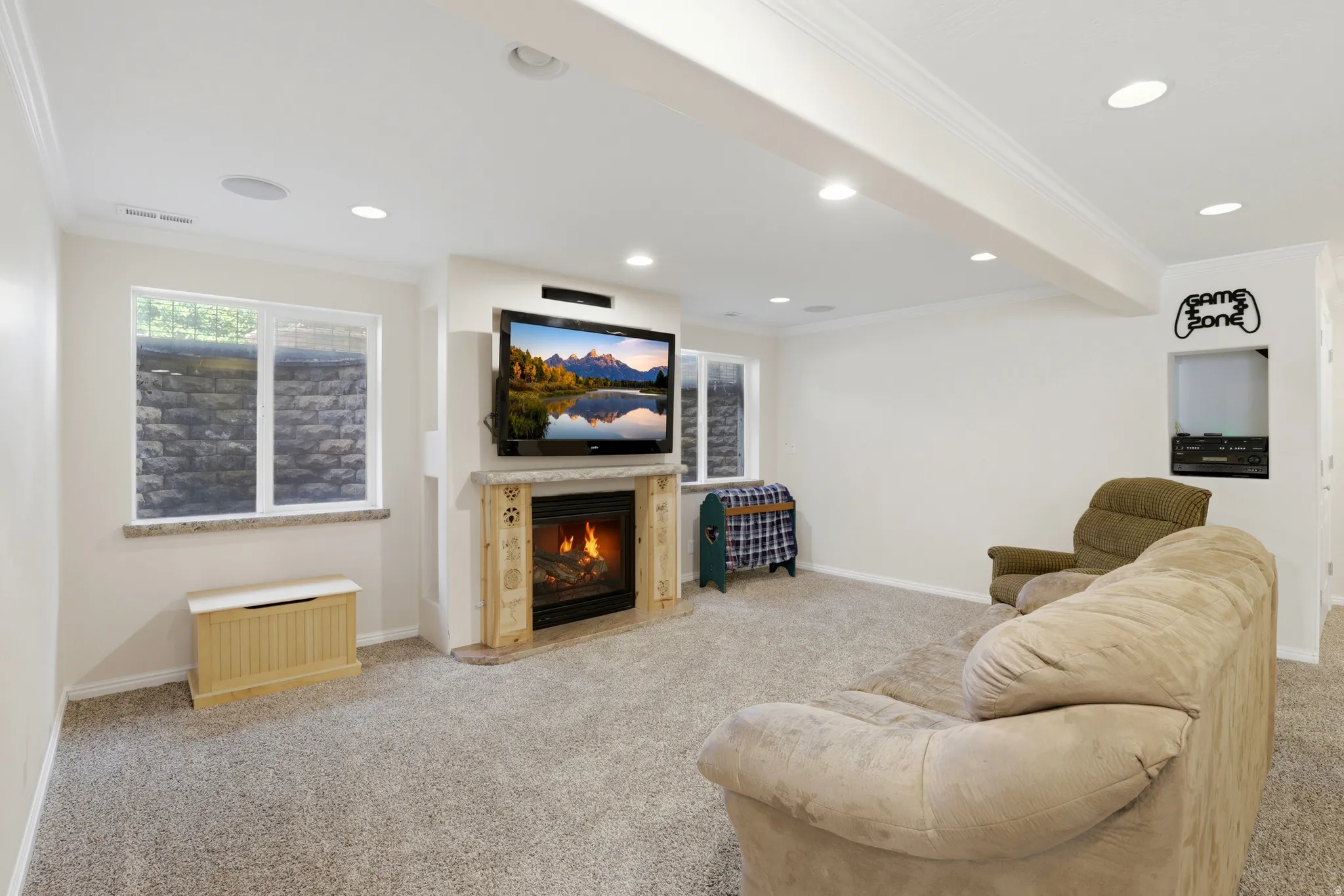 Spacious entertainment area featuring a built-in fireplace with a stone hearth, recessed lighting, carpeted flooring, and egress windows with stone well surrounds