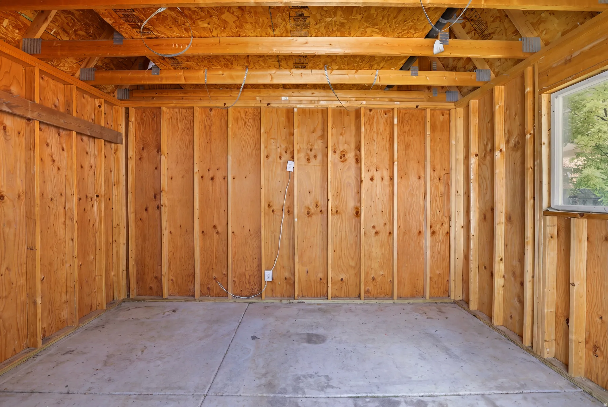 Unfinished interior space featuring exposed wood framing, wood paneling, a concrete floor, and a single window