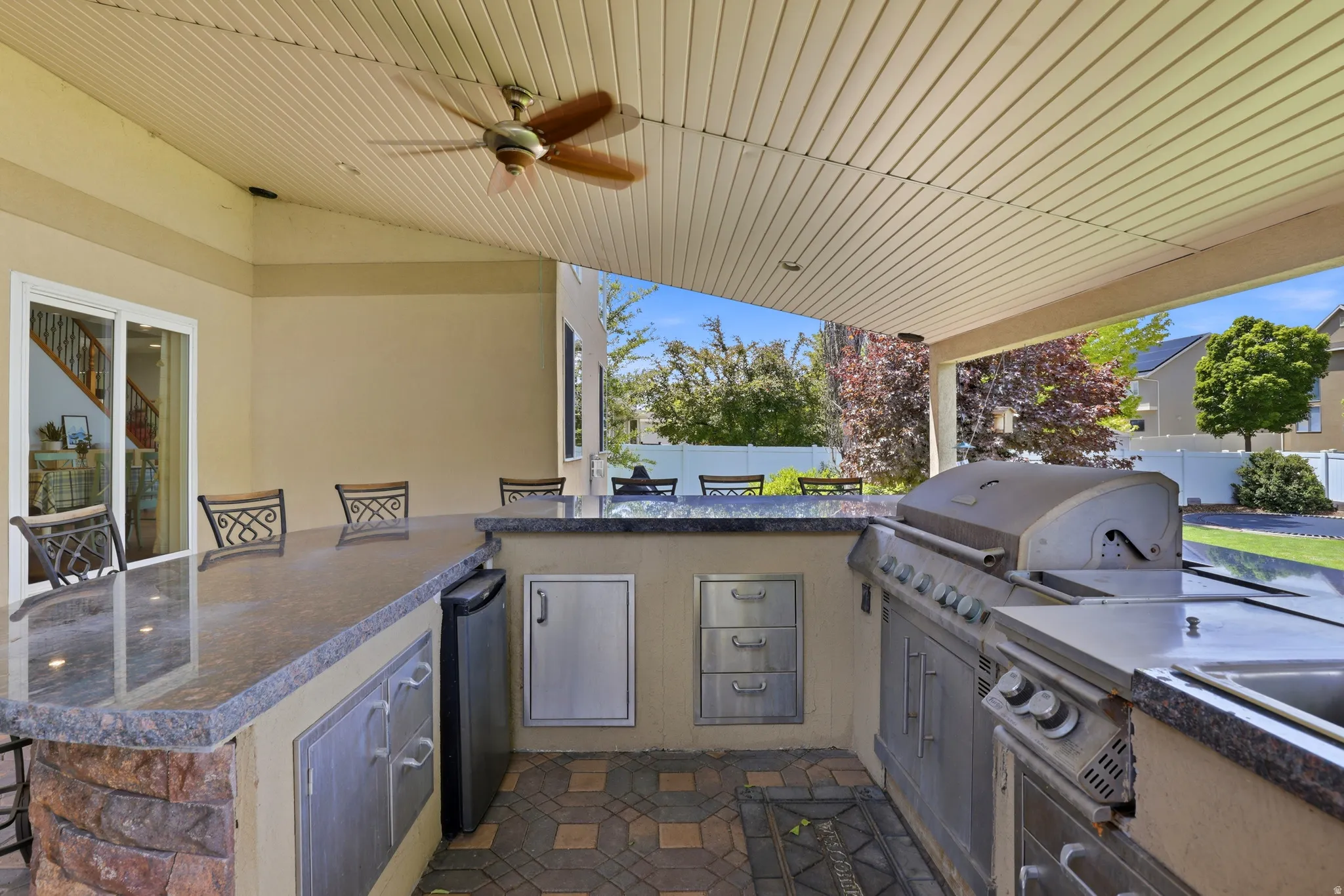 Outdoor kitchen featuring granite countertops, built-in stainless steel appliances, and a ceiling fan on a covered patio