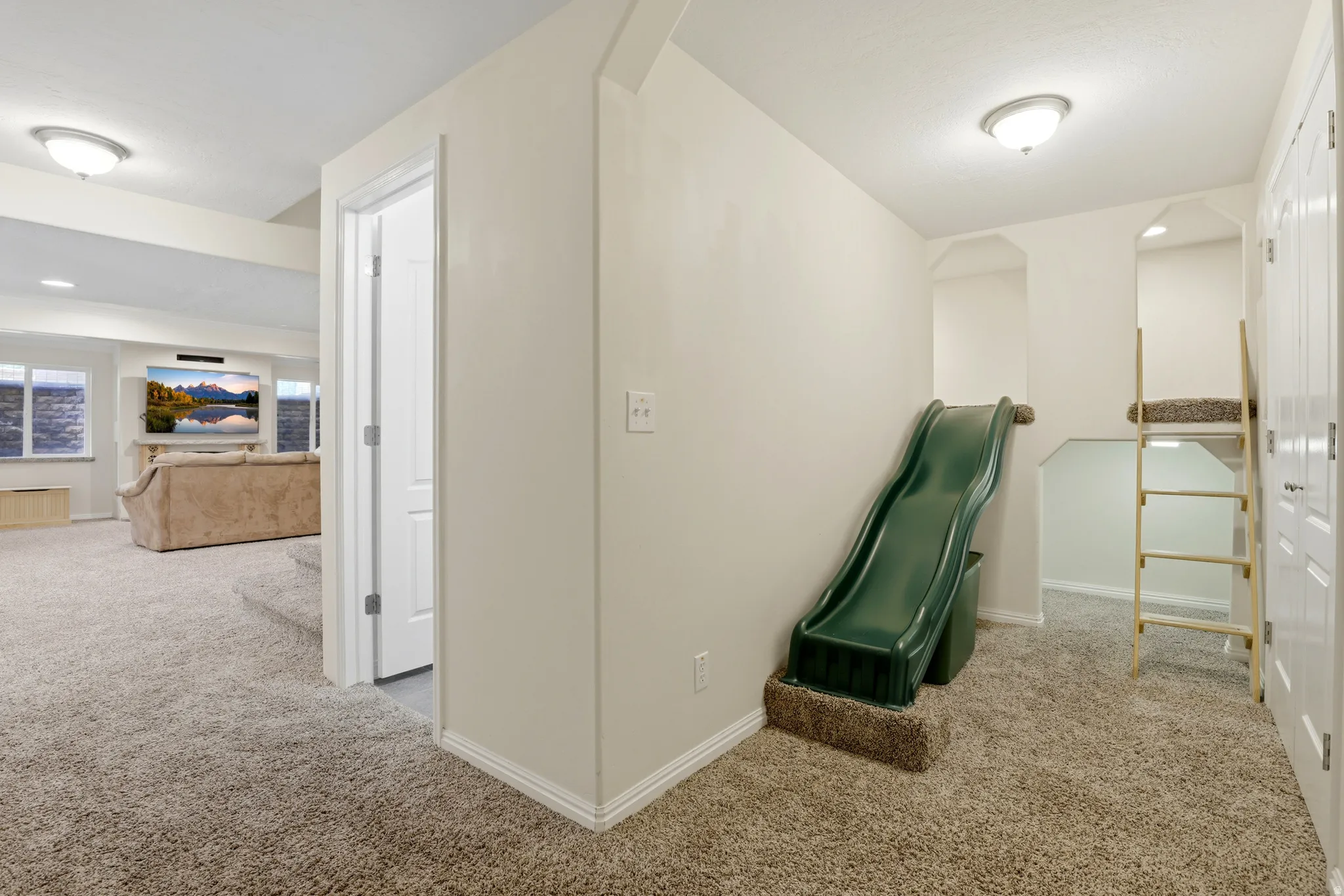 Carpeted hallway with a built-in slide, custom recessed bunk area with ladder, flush-mount lighting, and baseboard molding