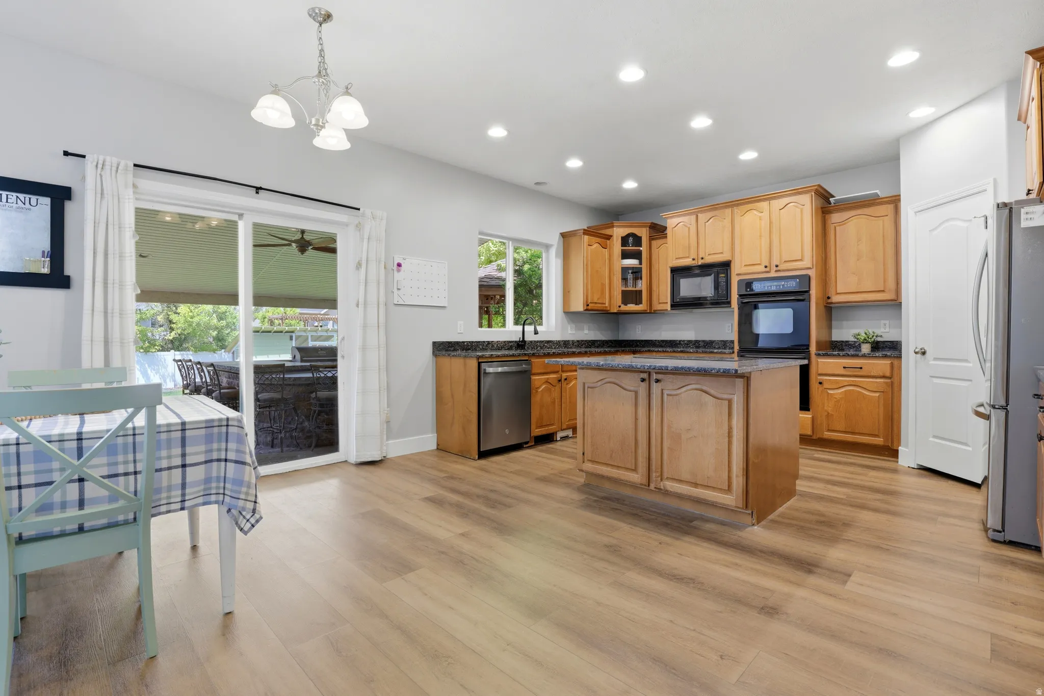 Open-concept kitchen featuring wood-finish flooring, light wood cabinetry, a kitchen island with storage, recessed lighting, and stainless steel appliances