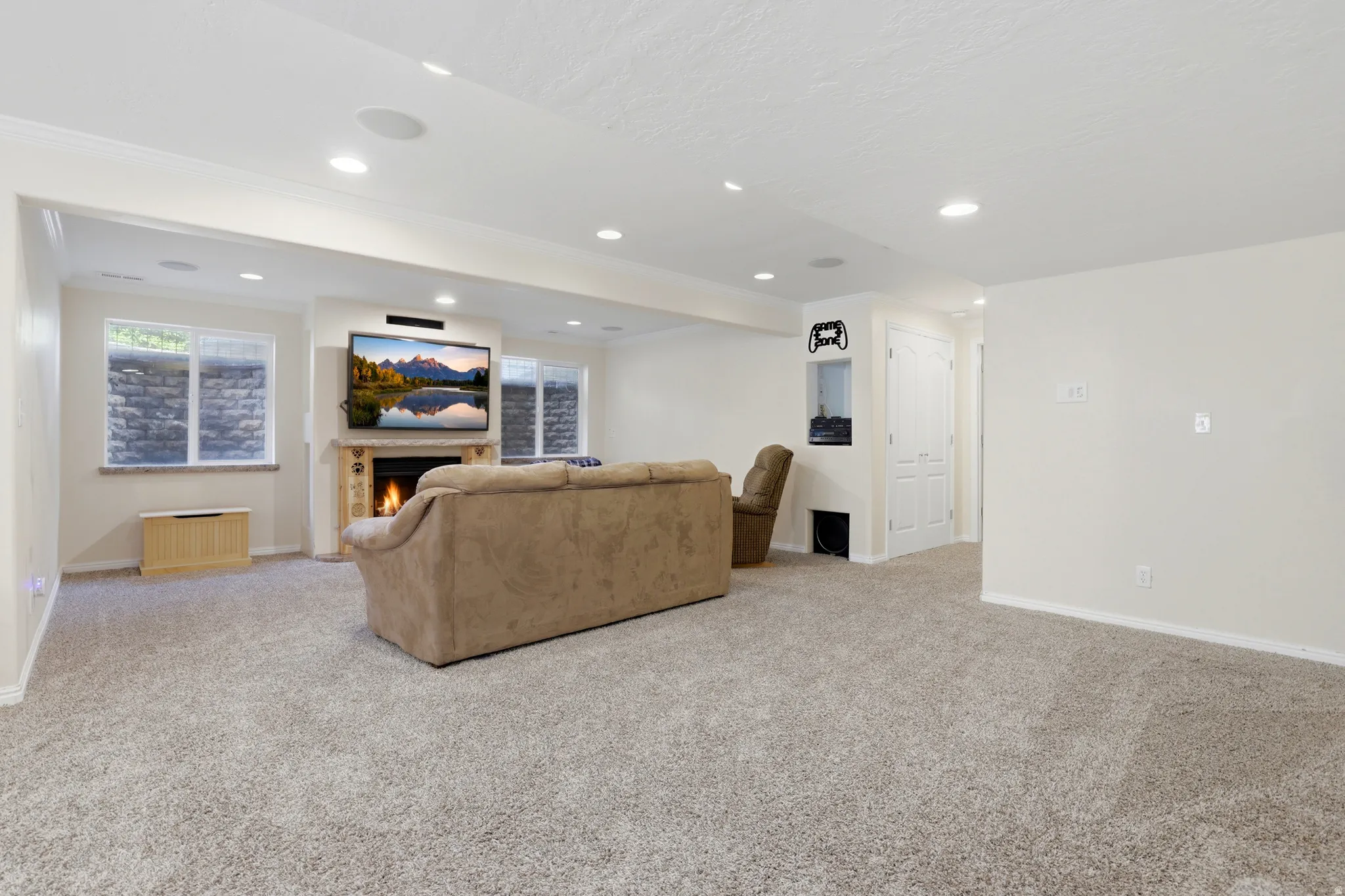 Spacious carpeted room featuring a stone-clad fireplace, built-in media niche, recessed lighting, and dual white trim windows