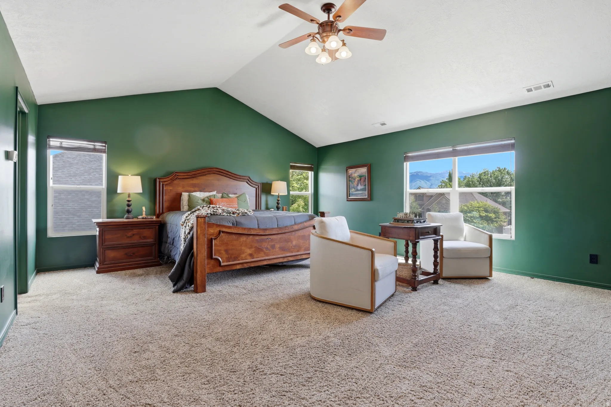 Spacious room featuring vaulted ceilings, a ceiling fan with integrated lighting, recessed windows with blinds, and light-toned carpeting