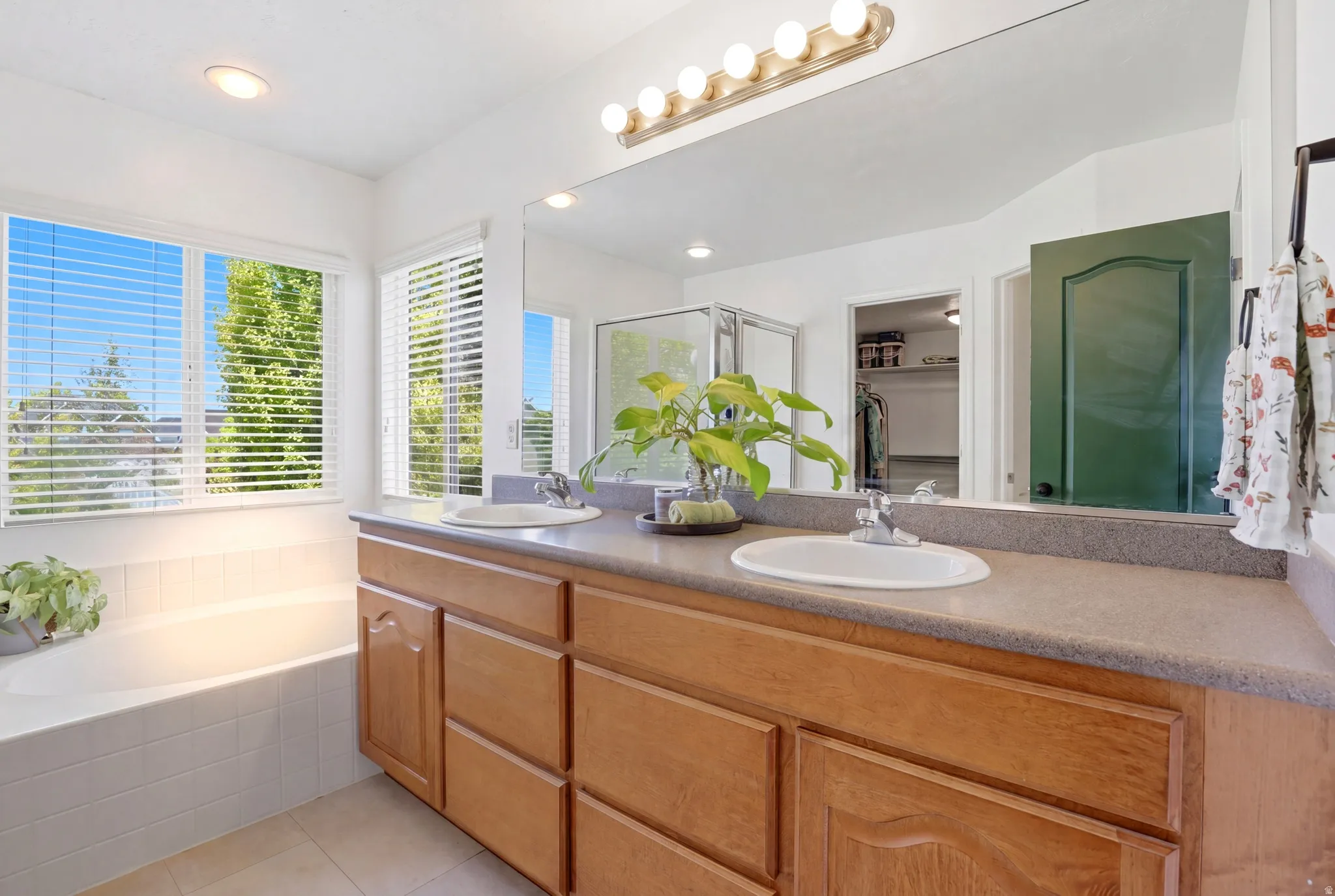 Spacious bathroom featuring a dual vanity with light-tone wood cabinetry, a built-in soaking tub with a tiled surround, a large mirror, and a standalone shower enclosure