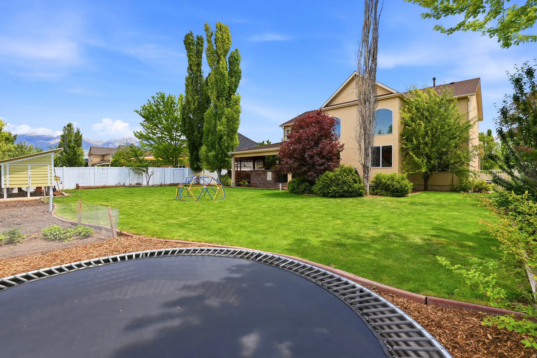 Spacious backyard featuring an expansive lawn, a raised garden bed with wood chip landscaping, and a white privacy fence