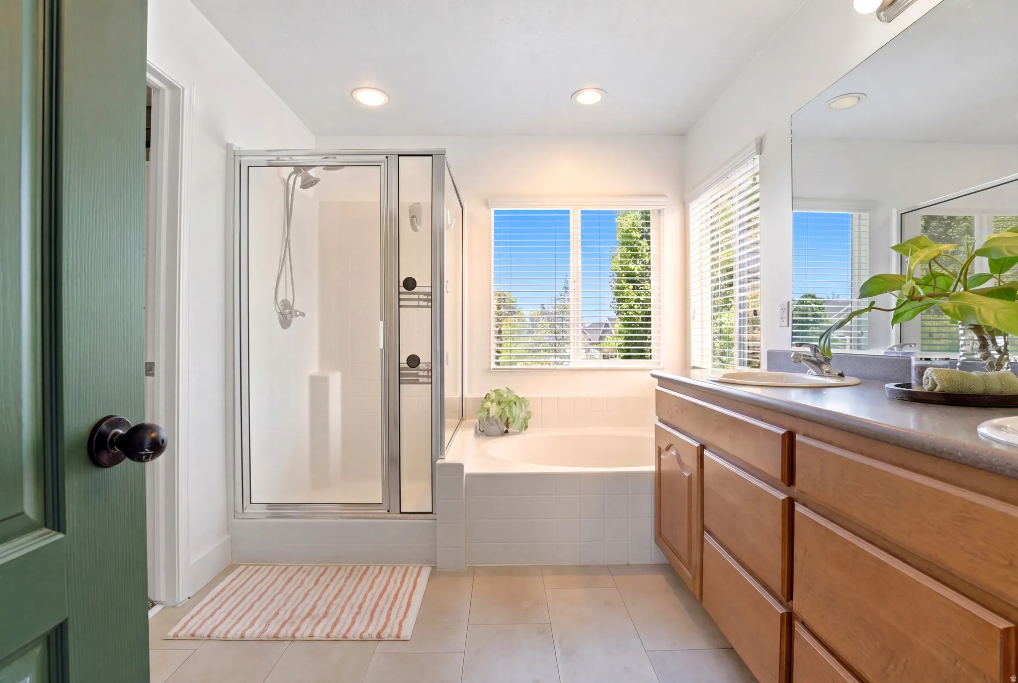 Full bathroom featuring a glass-enclosed shower, a built-in soaking tub beneath a window, a double vanity with wood cabinetry, and a large mirror