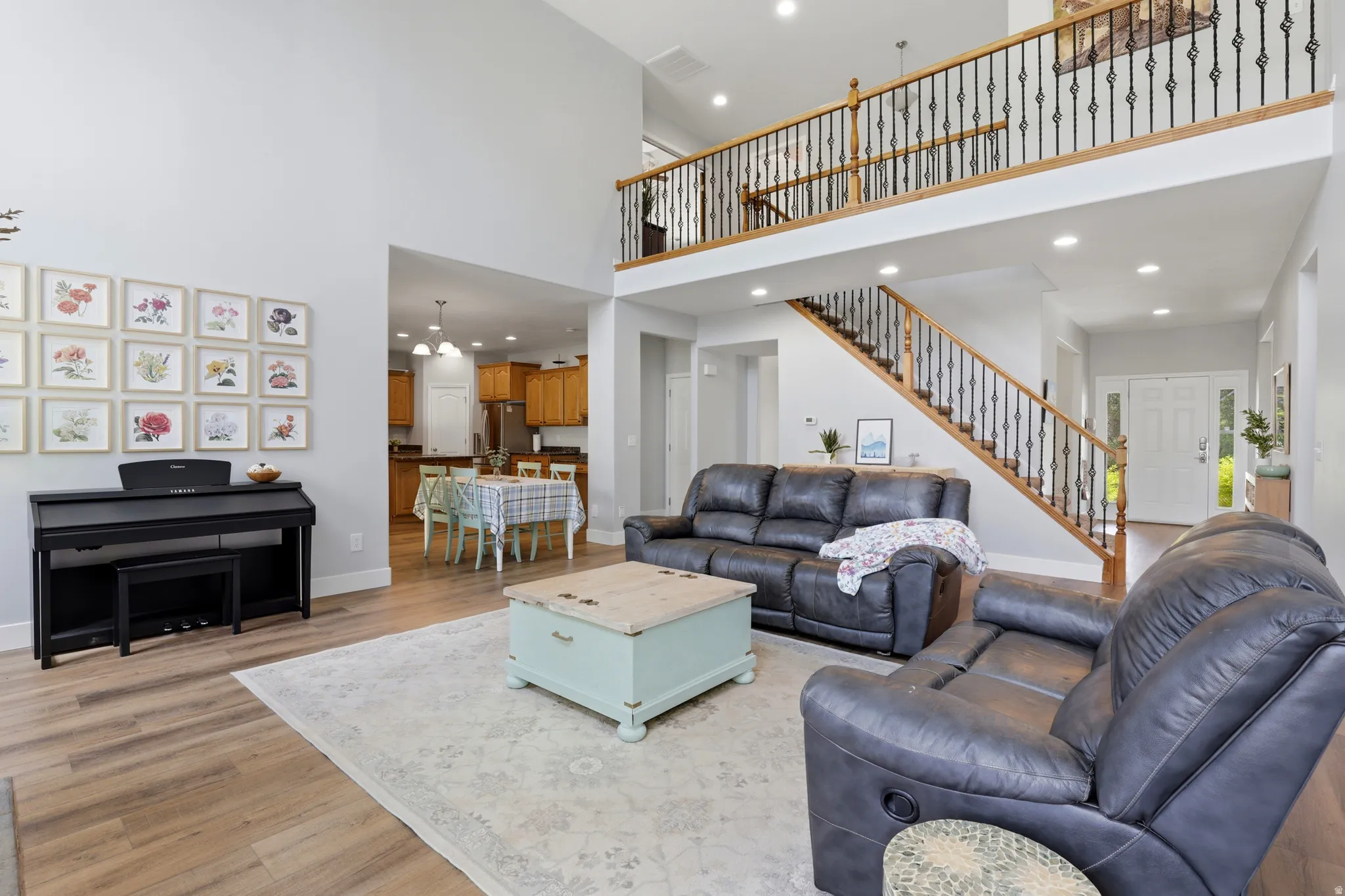 Two-story living area with wood-finish flooring, a grand staircase featuring dark iron balusters and a wood handrail, and an upper-level balcony