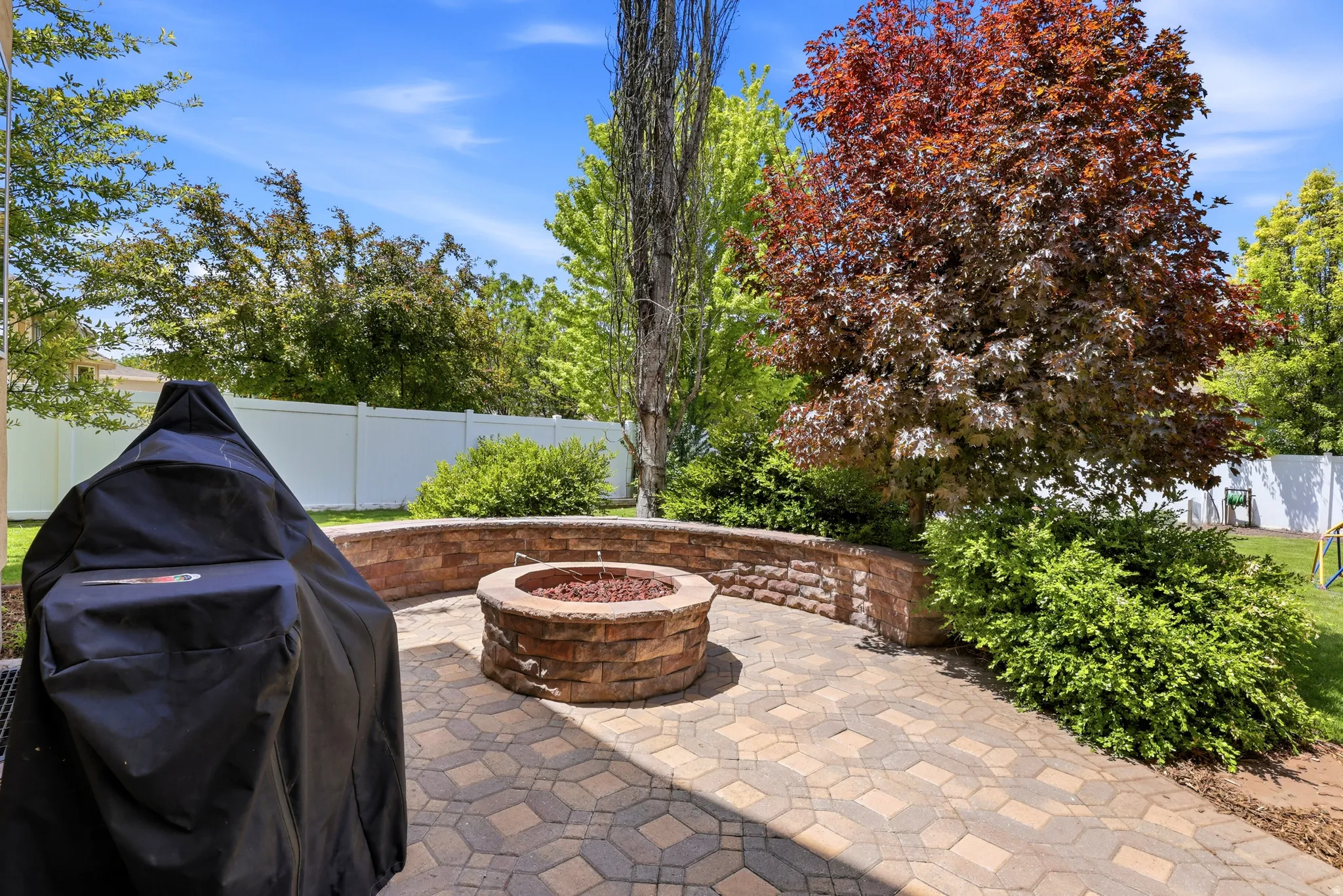 Paver patio featuring a built-in stone fire pit, a curved retaining wall, and mature landscaping