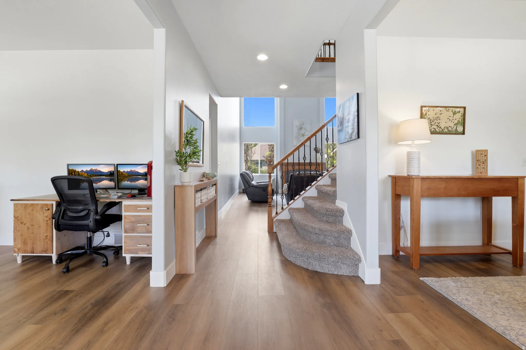 Spacious entryway featuring wood-finish flooring, a curved carpeted staircase with wrought iron balusters, and a dedicated workspace