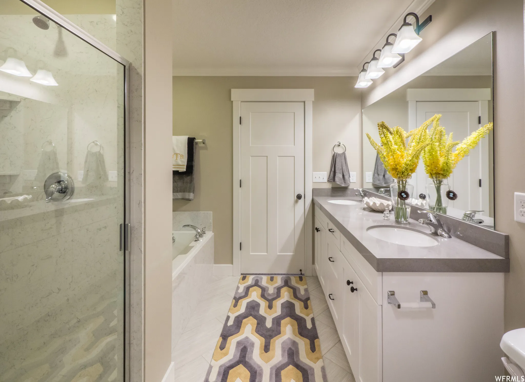 Full bath featuring crown molding, double vanity, a garden tub, light tile patterned flooring, and a shower stall