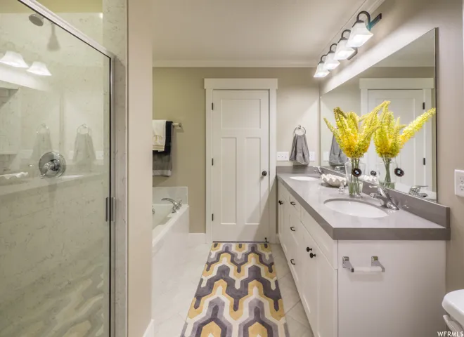 Full bath featuring crown molding, double vanity, a garden tub, light tile patterned flooring, and a shower stall