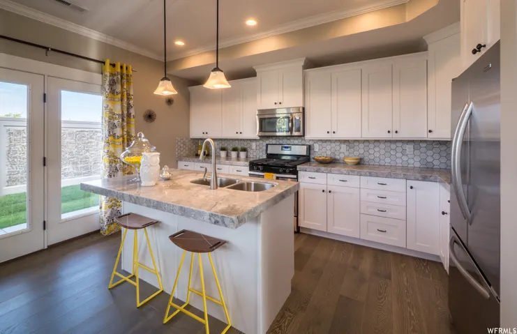 Kitchen featuring white cabinetry, stainless steel appliances, a center island with sink, dark wood finished floors, and crown molding