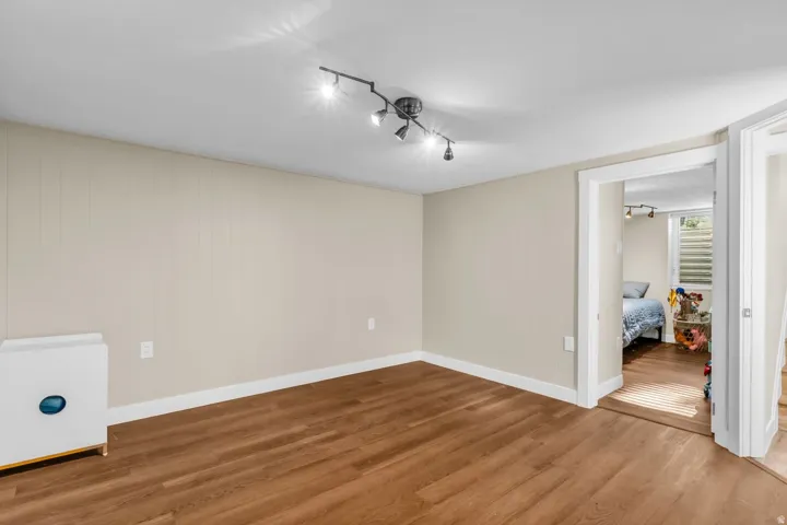 Expansive room featuring wood-finish flooring, light neutral paneling, track lighting, and white baseboards