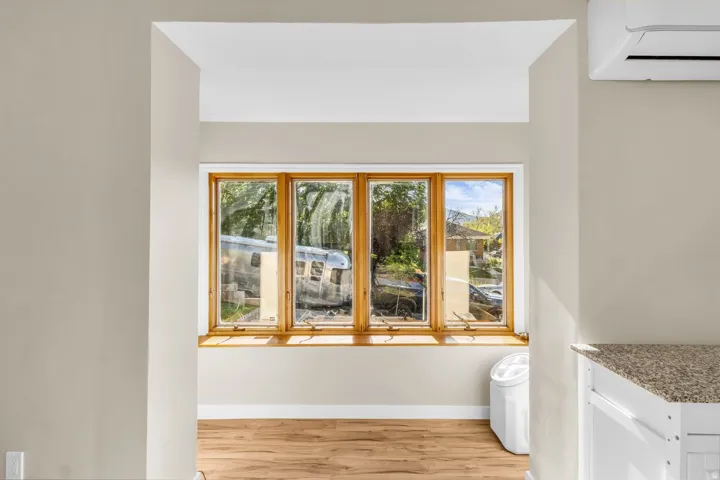 Bay window with natural wood trim, light wood-finish flooring, neutral wall paint, and a wall-mounted mini-split system