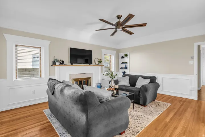 Living room featuring wood-finish flooring, a white fireplace with a mantel, and wainscoting