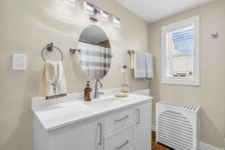 Contemporary bathroom featuring a white vanity with a solid surface countertop, an oval mirror, and a window with white blinds