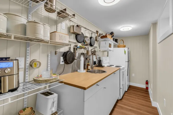 Compact kitchen featuring a stainless steel sink, wood-finish countertop, and white cabinetry
