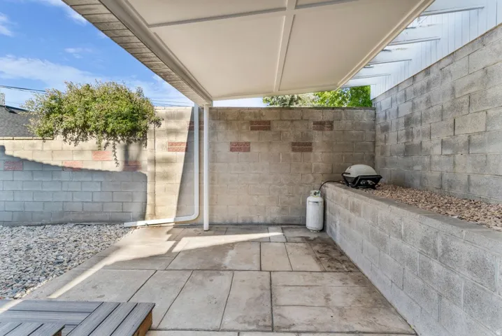 Outdoor patio area featuring concrete paver flooring, a white overhead pergola structure, and surrounding concrete block walls
