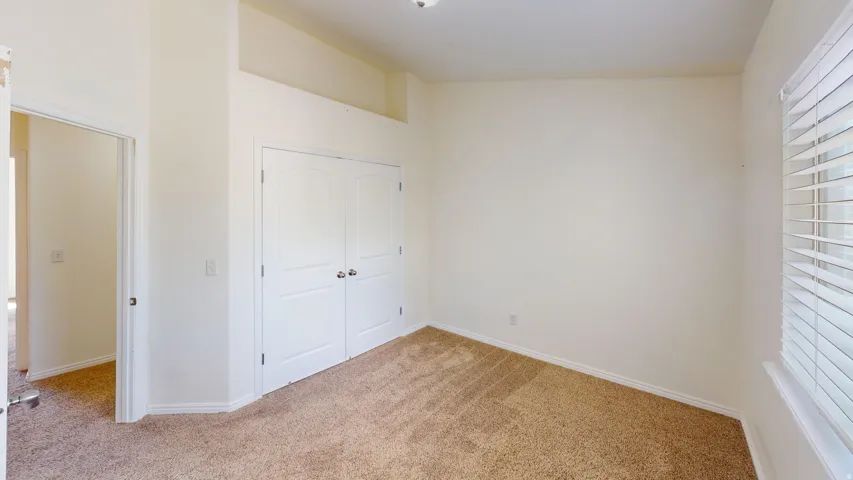 Spacious room featuring neutral carpeting, a window with blinds, and white bi-fold doors
