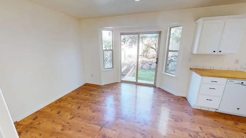 Wood-finish flooring, white cabinetry with dark hardware, wood-finish countertop, subway tile backsplash, and a sliding glass door to the exterior