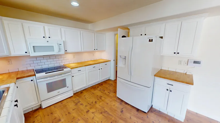 Updated kitchen featuring white shaker-style cabinetry, wood-finish countertops, white subway tile backsplash, and wood-look flooring