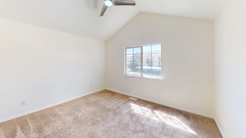 Vaulted ceilings with a ceiling fan, plush carpeting, and a large window