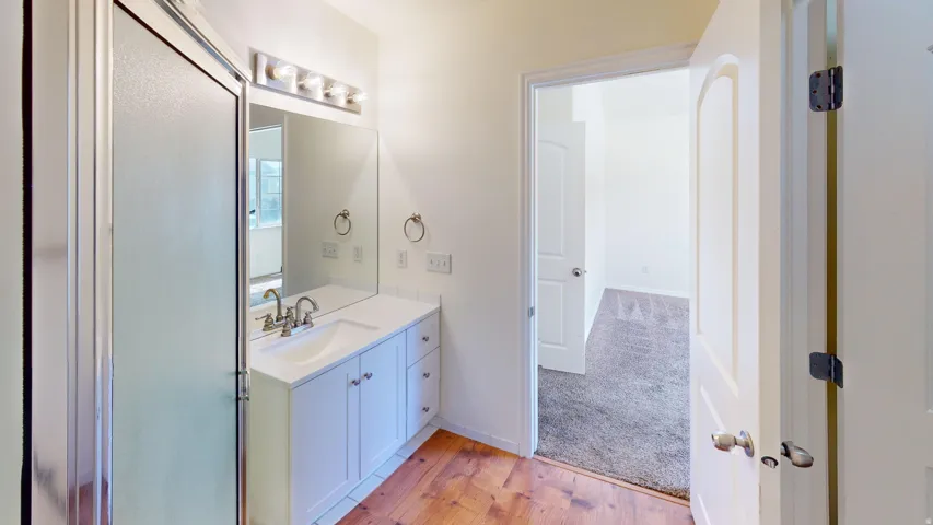 Bathroom featuring a white vanity with an integrated sink, polished chrome faucet, a rectangular mirror, and a shower with a sliding frosted glass door