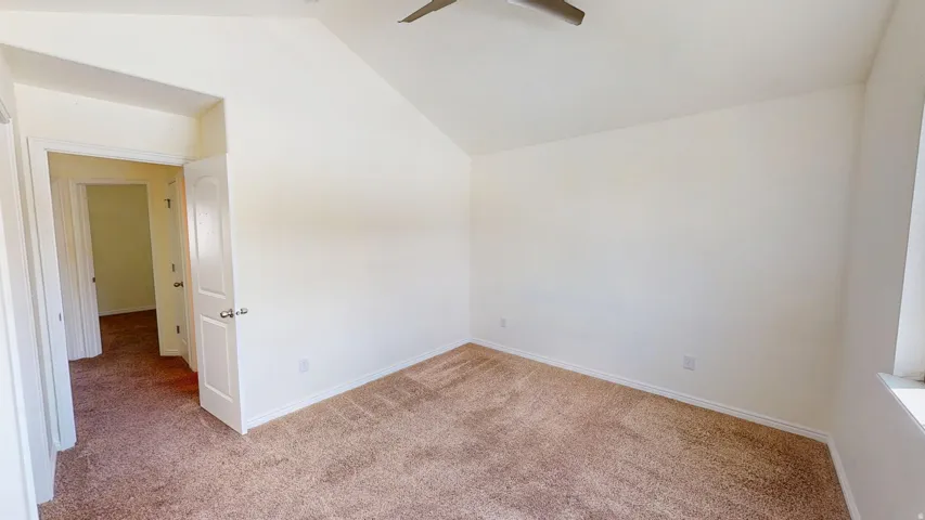 Vaulted ceiling, ceiling fan, neutral carpet, white interior doors, and a window with a sill