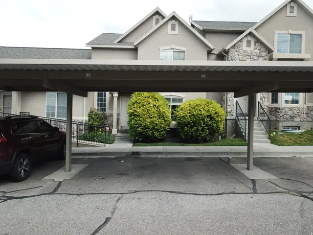 Carport parking space with townhouse exterior featuring stone accents and mature landscaping