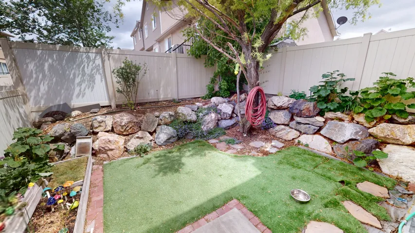 Backyard featuring artificial turf, a rock retaining wall, a raised garden bed with brick trim, and a mature tree