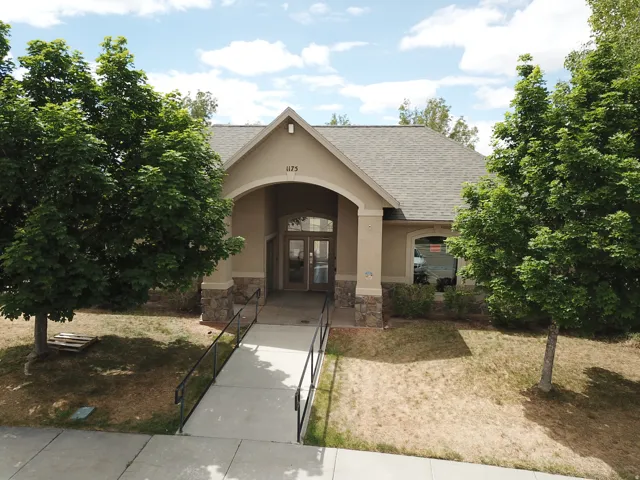 Building exterior featuring a stucco finish with stone accents, an arched entry, a paved walkway, and mature trees