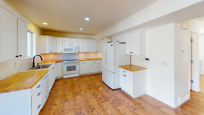 Spacious kitchen featuring extensive white cabinetry, wood-finish countertops, subway tile backsplash, and wood-finish flooring